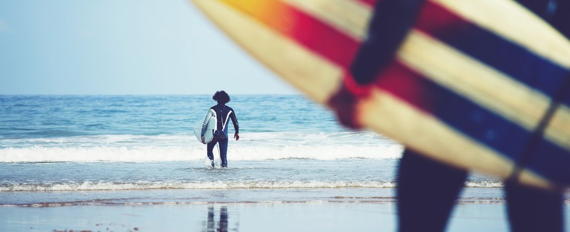 Professional surfers carrying their surfboards while going to the sea, professional surfers in black diving suits ready to surf walk to the ocean, close up of surfboard with surfer on background