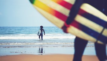 Professional surfers carrying their surfboards while going to the sea, professional surfers in black diving suits ready to surf walk to the ocean, close up of surfboard with surfer on background