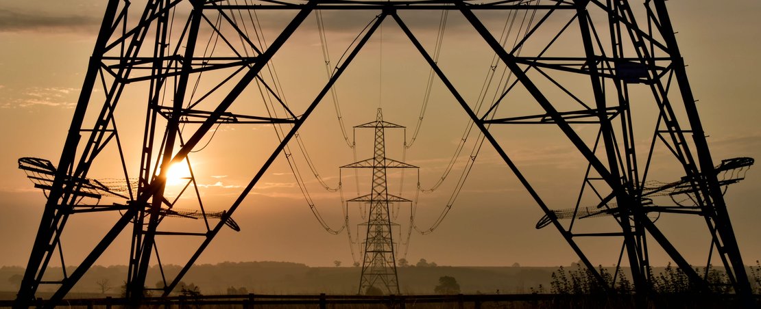 Silhouette of a power line against a vibrant sunset sky, showcasing hues of orange and purple.
