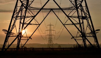 Silhouette of a power line against a vibrant sunset sky, showcasing hues of orange and purple.