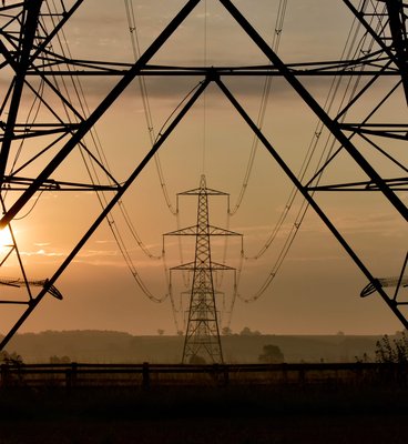 Silhouette of a power line against a vibrant sunset sky, showcasing hues of orange and purple.