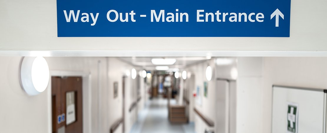 A hospital hallway featuring a blue sign indicating the way out to the main entrance.