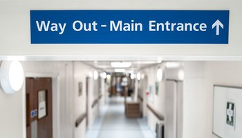 A hospital hallway featuring a blue sign indicating the way out to the main entrance.