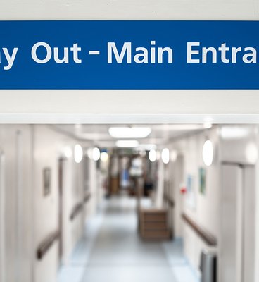 A hospital hallway featuring a blue sign indicating the way out to the main entrance.