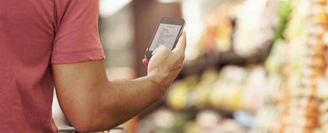 Close Up Of Man Reading Shopping List From Mobile Phone In Supermarket
