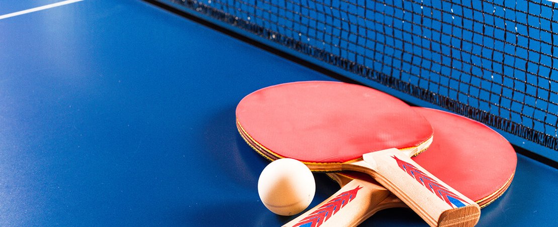 A table tennis racket and a ball resting on a blue table surface.