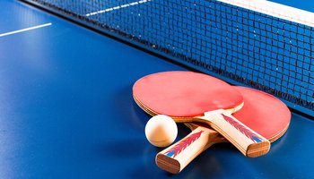 A table tennis racket and a ball resting on a blue table surface.