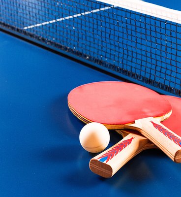 A table tennis racket and a ball resting on a blue table surface.