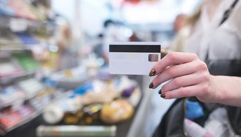 Hand with a white credit card on the background of a supermarket