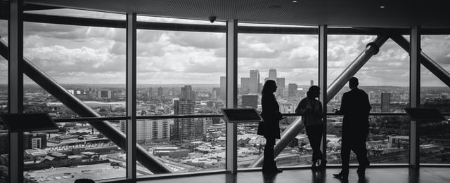 People meeting near large window with city views