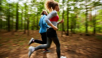 Young couple in activewear running on forest road with blurry trees on background