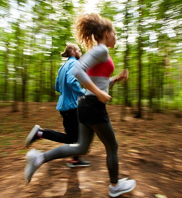 Young couple in activewear running on forest road with blurry trees on background